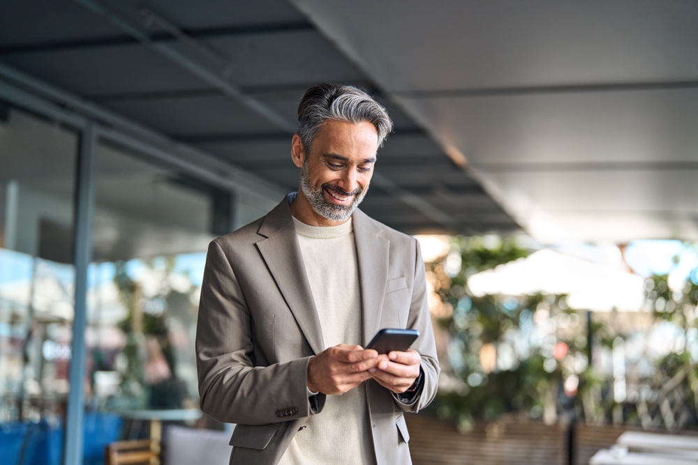 Happy,Mature,Older,Male,Entrepreneur,Standing,Outdoors,Looking,At,Smartphone.